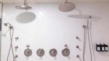 Un baño con pared de azulejos blancos en patrón de espiga, un cabezal de ducha, una ducha de mano, un grifo empotrado y tres botellas de champú.