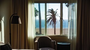 A room with a view of the beach, a chair, a lamp, and a small table. - The Eden (Santa Monica)