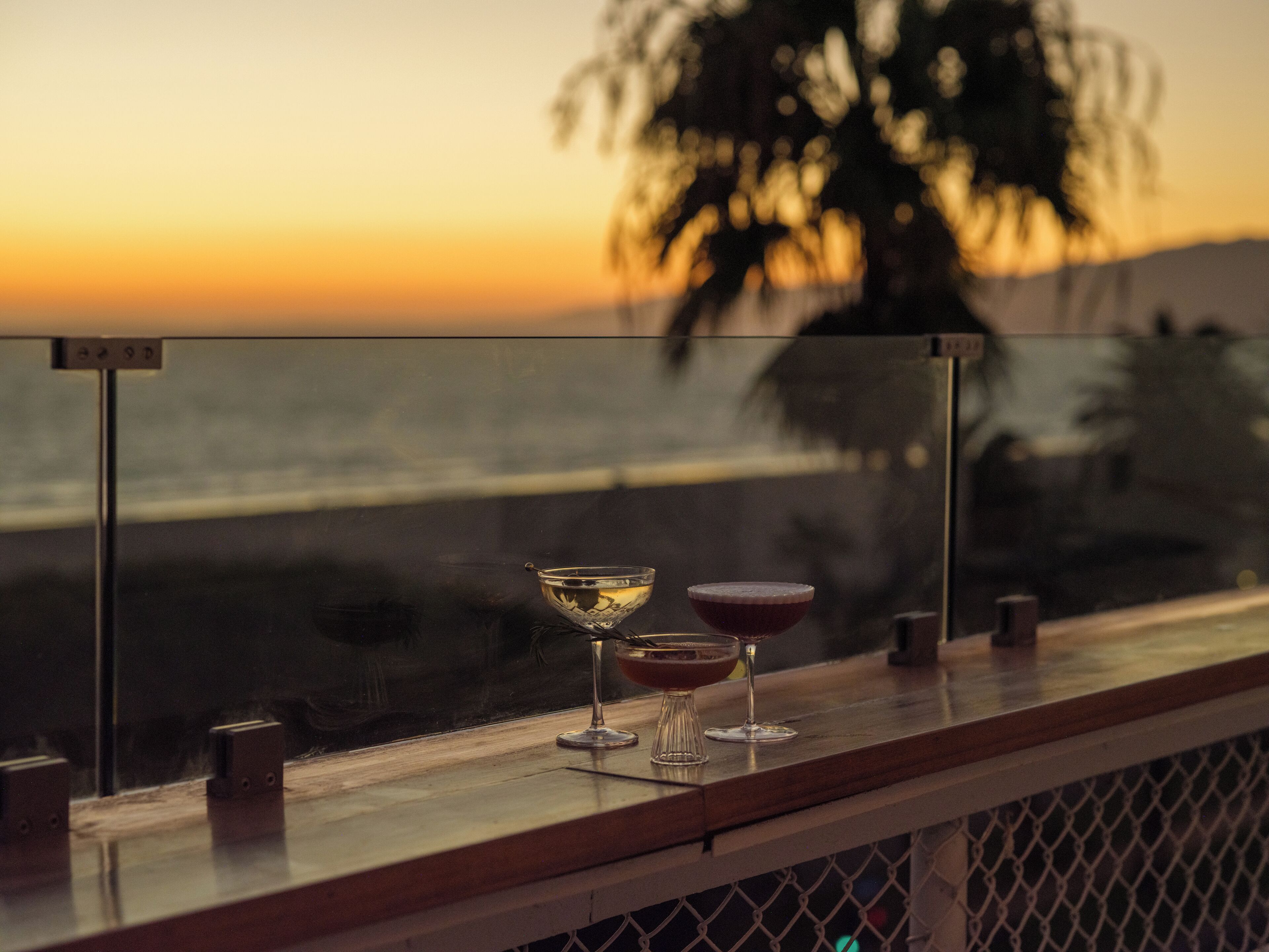 A bar with two glasses of drink and a glass of water on a wooden counter.