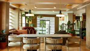 A spacious dining area with a central table, multiple chairs, hanging plants, and a view of the outdoors. - The Eden (Santa Monica)