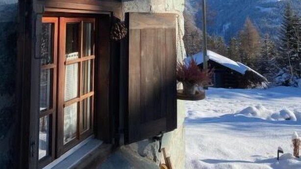 Une cabane en bois avec une façade en pierre, une porte en bois et un banc à l’extérieur.