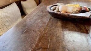 Une table de salle à manger en bois, sur laquelle se trouve un saladier rempli de fruits, et un luminaire suspendu au plafond.