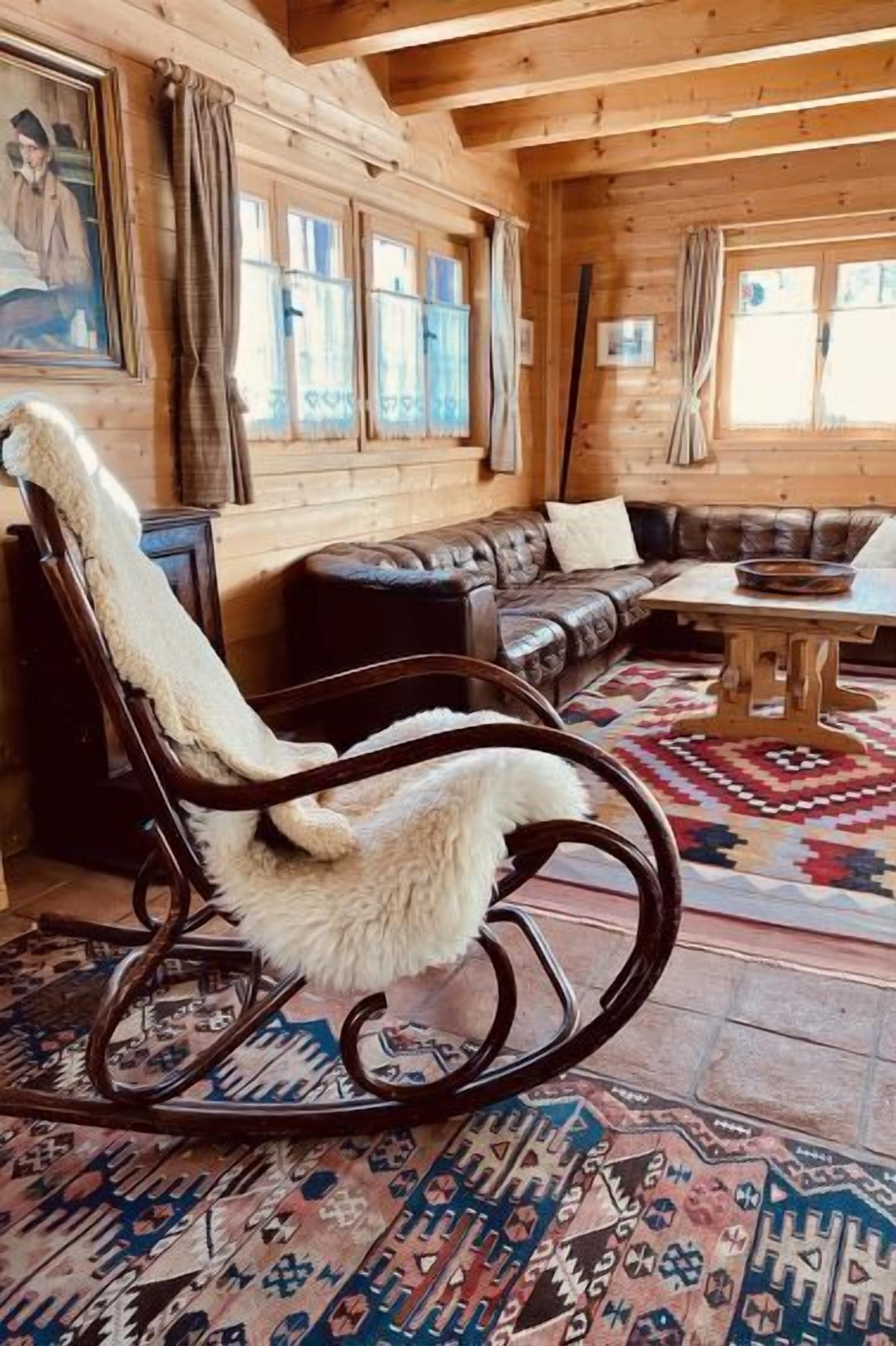L’intérieur d’un chalet en bois, avec un fauteuil à bascule, un canapé en cuir et un tapis à motifs.