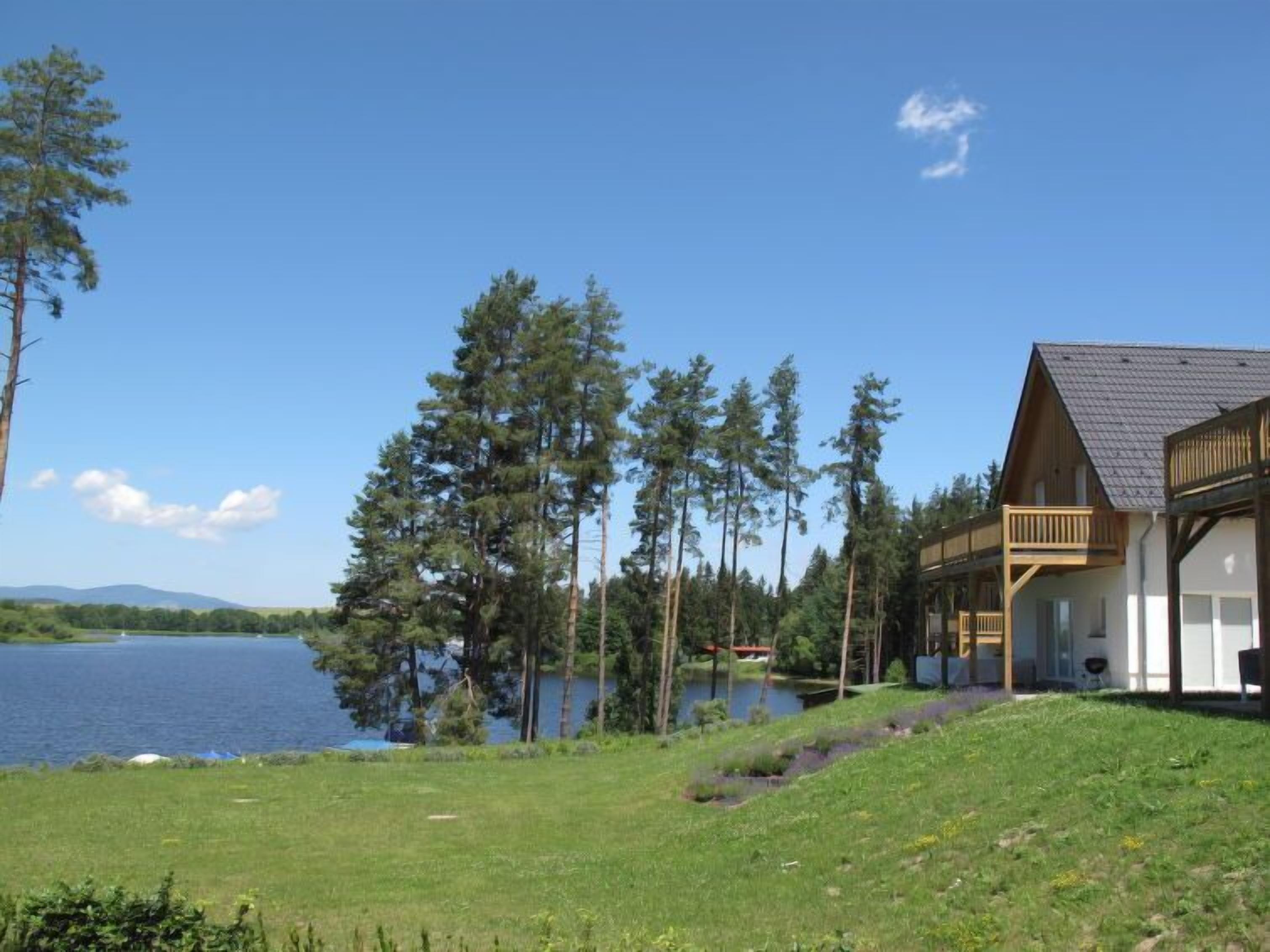 A lakeside cabin with a deck overlooking the water, surrounded by tall trees.