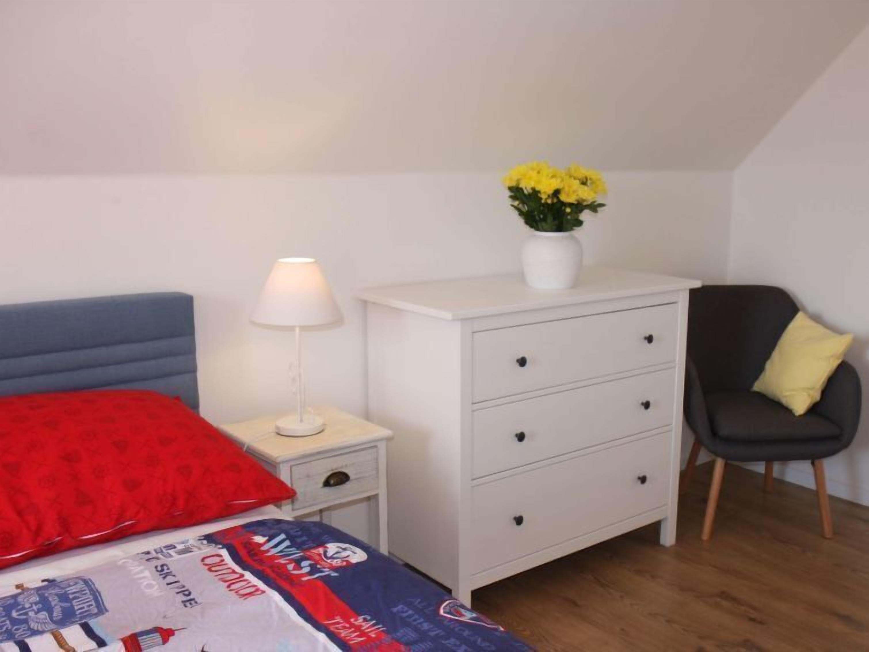 A bedroom with a bed, a nightstand with a lamp, a dresser, and a chair.