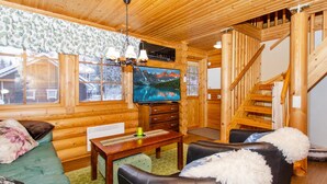 A cozy log cabin interior with a wooden staircase, a television, a dining area, and a sofa.