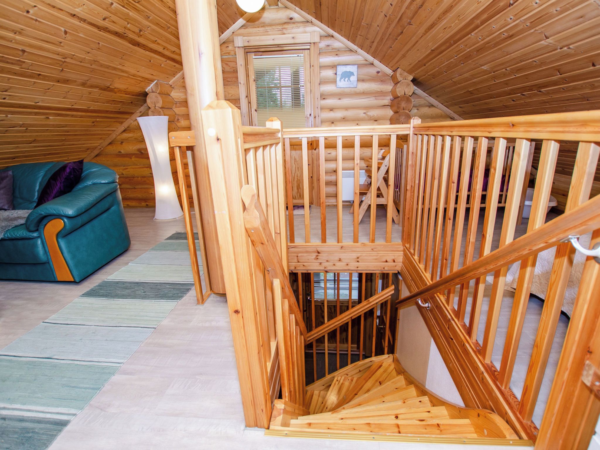 Un interior de madera con una escalera que sube a un nivel superior, un sofá y un símbolo de oso en la pared.