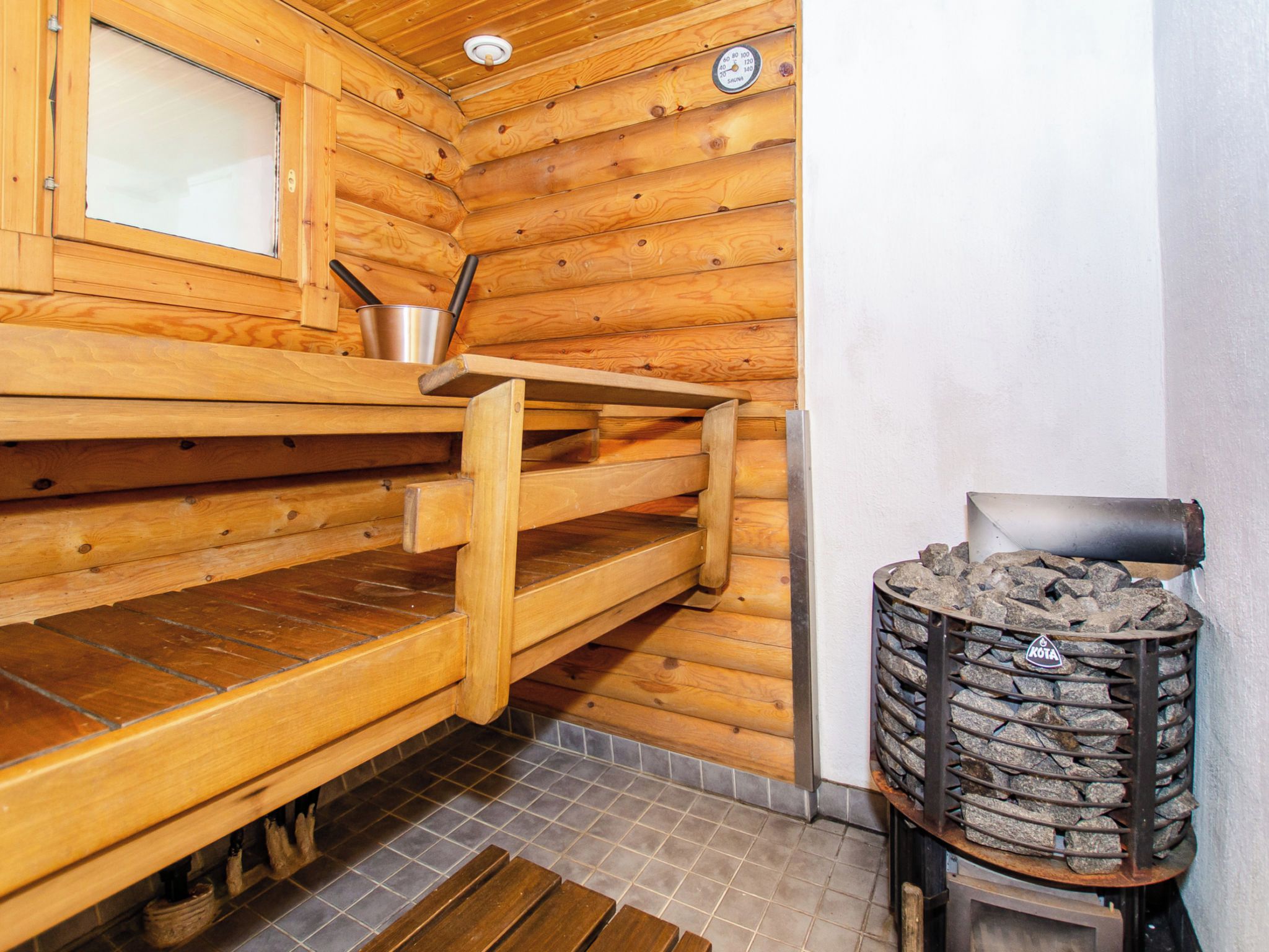 A sauna room with wooden benches, a metal bucket, and a stone-filled container.