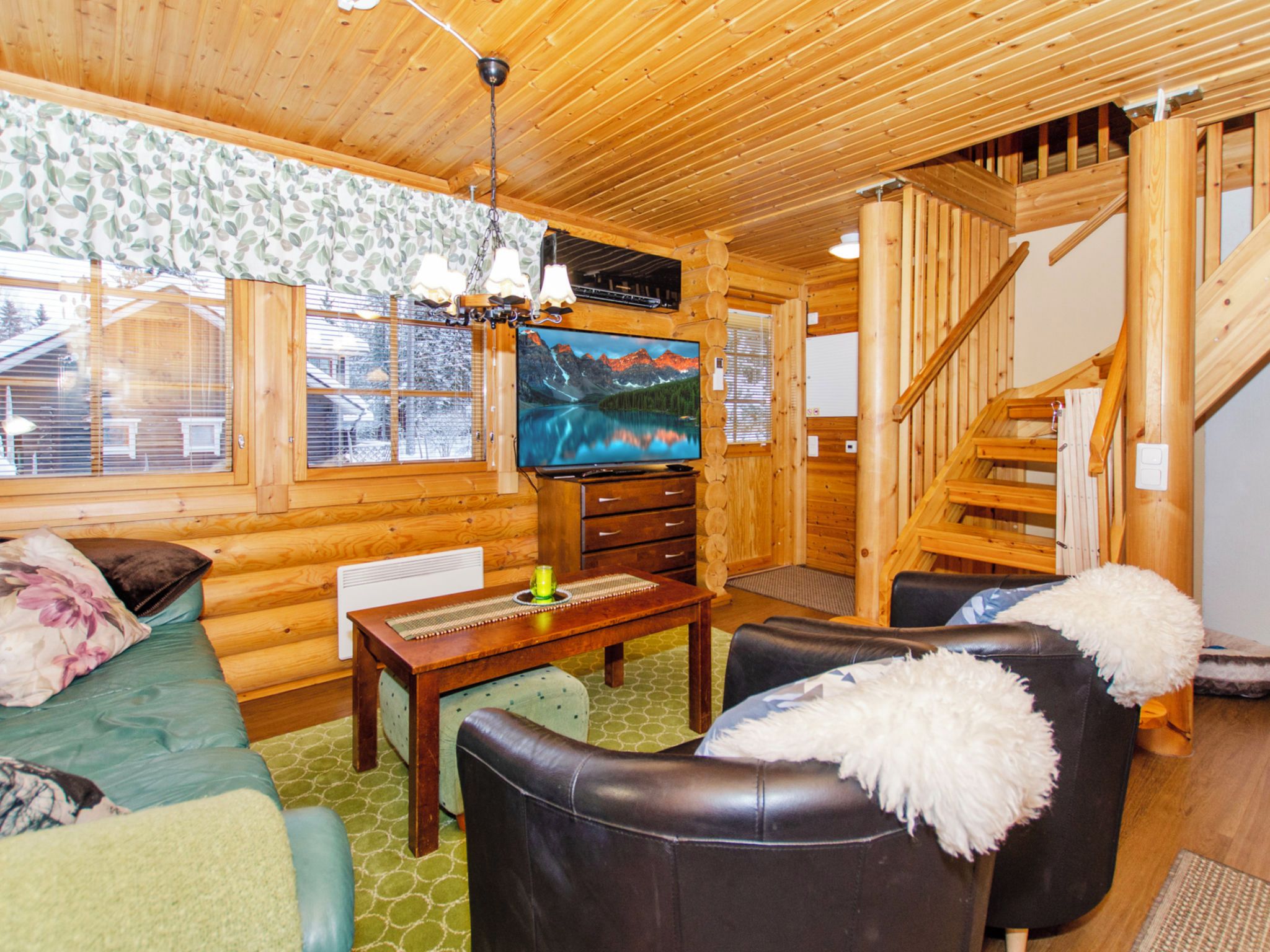 A cozy log cabin interior with a wooden staircase, a television, and a fireplace.