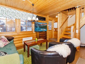 A cozy log cabin interior with a wooden staircase, a television, and a fireplace.