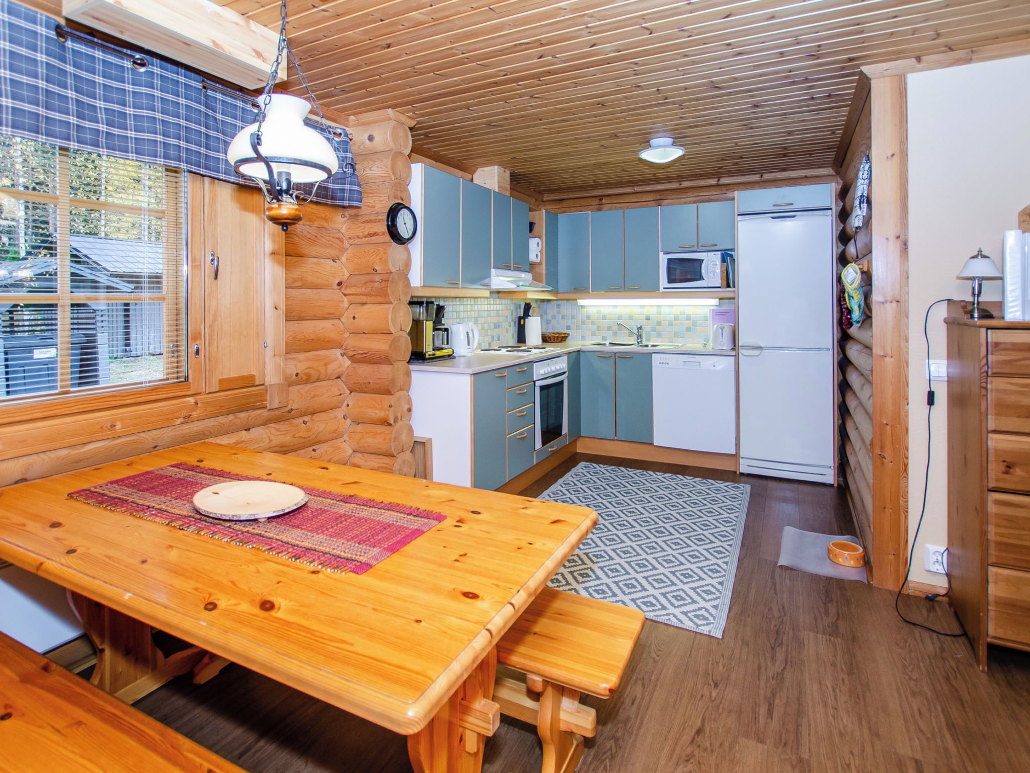 Una cocina acogedora de estilo cabaña, con armarios de madera, una mesa con bancos y una ventana que da a un jardín.