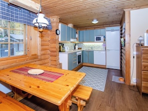 A cozy cabin-style kitchen with wooden cabinets, a dining table with benches, and a window overlooking a garden.