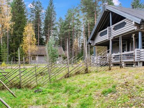 A log cabin with a porch and a fenced area with wooden stakes.
