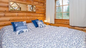 A log cabin room with a bed, a mirror, and a window with curtains.