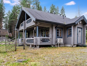 A log cabin with a porch, a chimney, and a window with a view of the surrounding forest.