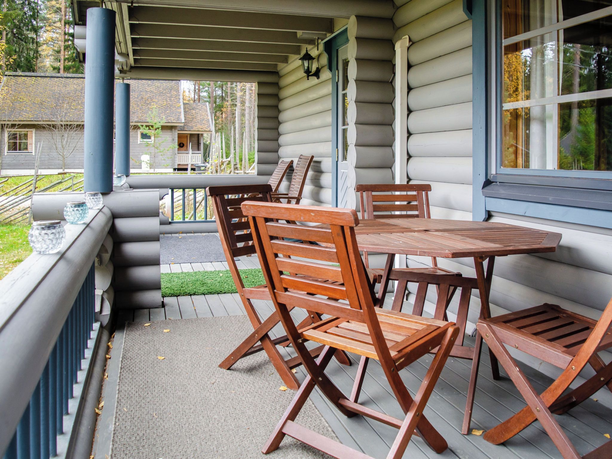 A covered outdoor seating area with a table and chairs, a view of the surrounding landscape, and a building with log siding.