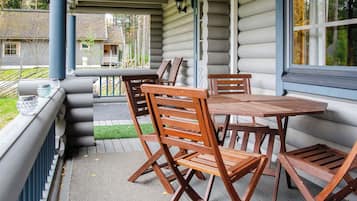 A covered outdoor seating area with a table and chairs, a view of the surrounding landscape, and a building with log siding.