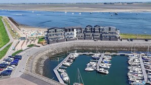 Un puerto deportivo con barcos amarrados, un edificio de varios pisos y una zona de playa arenosa con gente.