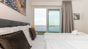 Habitación de hotel con una cama grande, una cama más pequeña, vista al mar y un cuadro en la pared.
