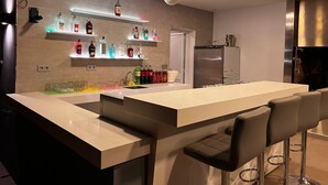 A modern kitchen with a central island, bar stools, a refrigerator, and shelves with various bottles.