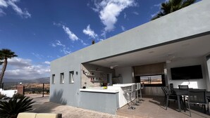 A modern outdoor kitchen area with a bar, seating, and a TV.