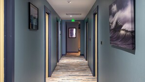 A hallway with wooden flooring, framed artwork on the walls, and doors leading to rooms.
