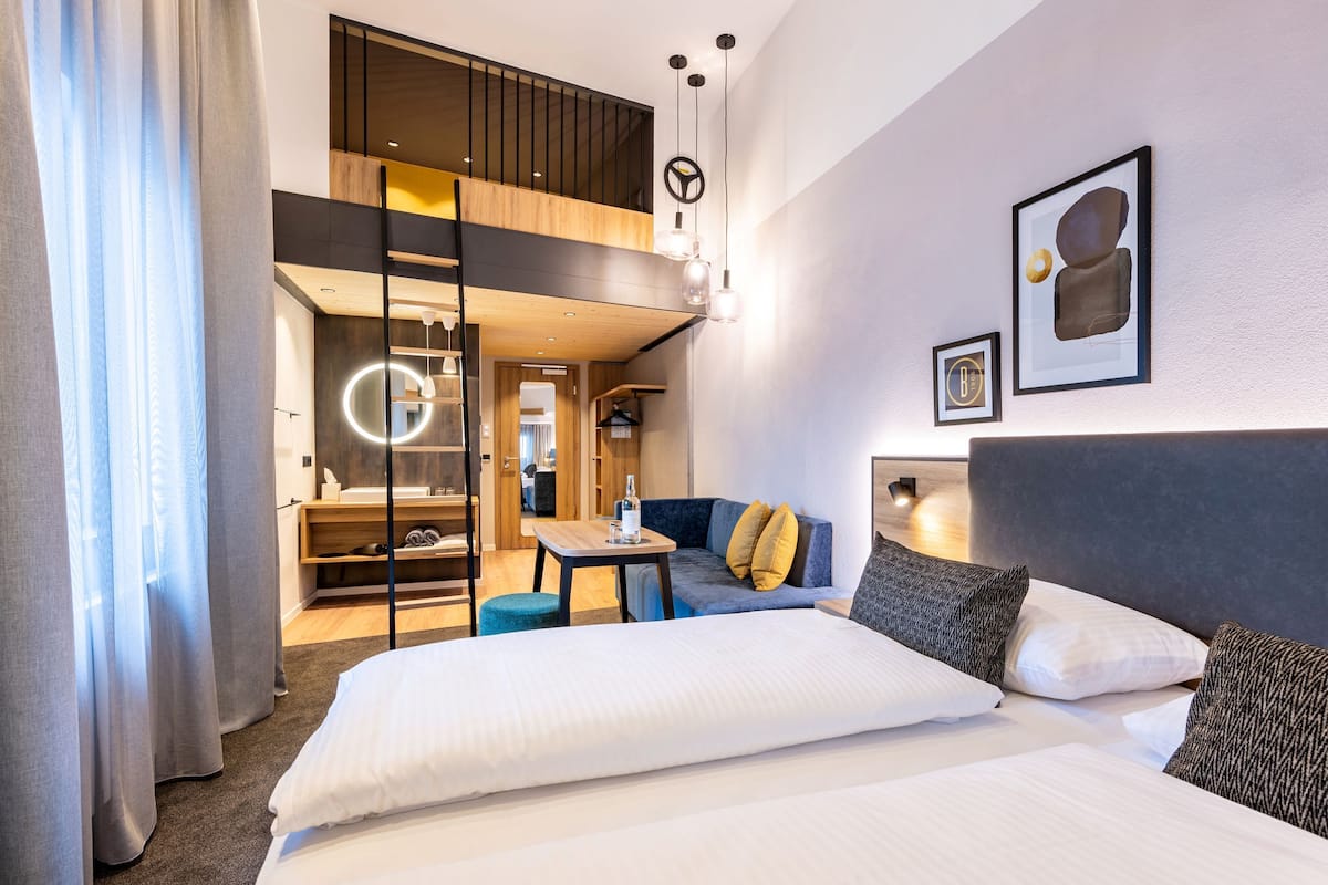 A modern hotel room with a large bed, a sofa, a desk, and a view of the interior.