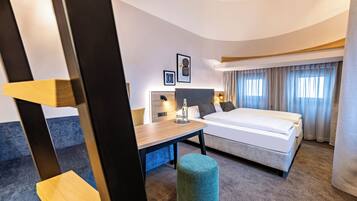 Ein modernes Hotelzimmer mit Bett, Schreibtisch, Stuhl und rundem Pouf.
