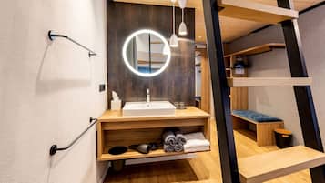 Un baño moderno con un espejo redondo, un lavamanos y un banco.