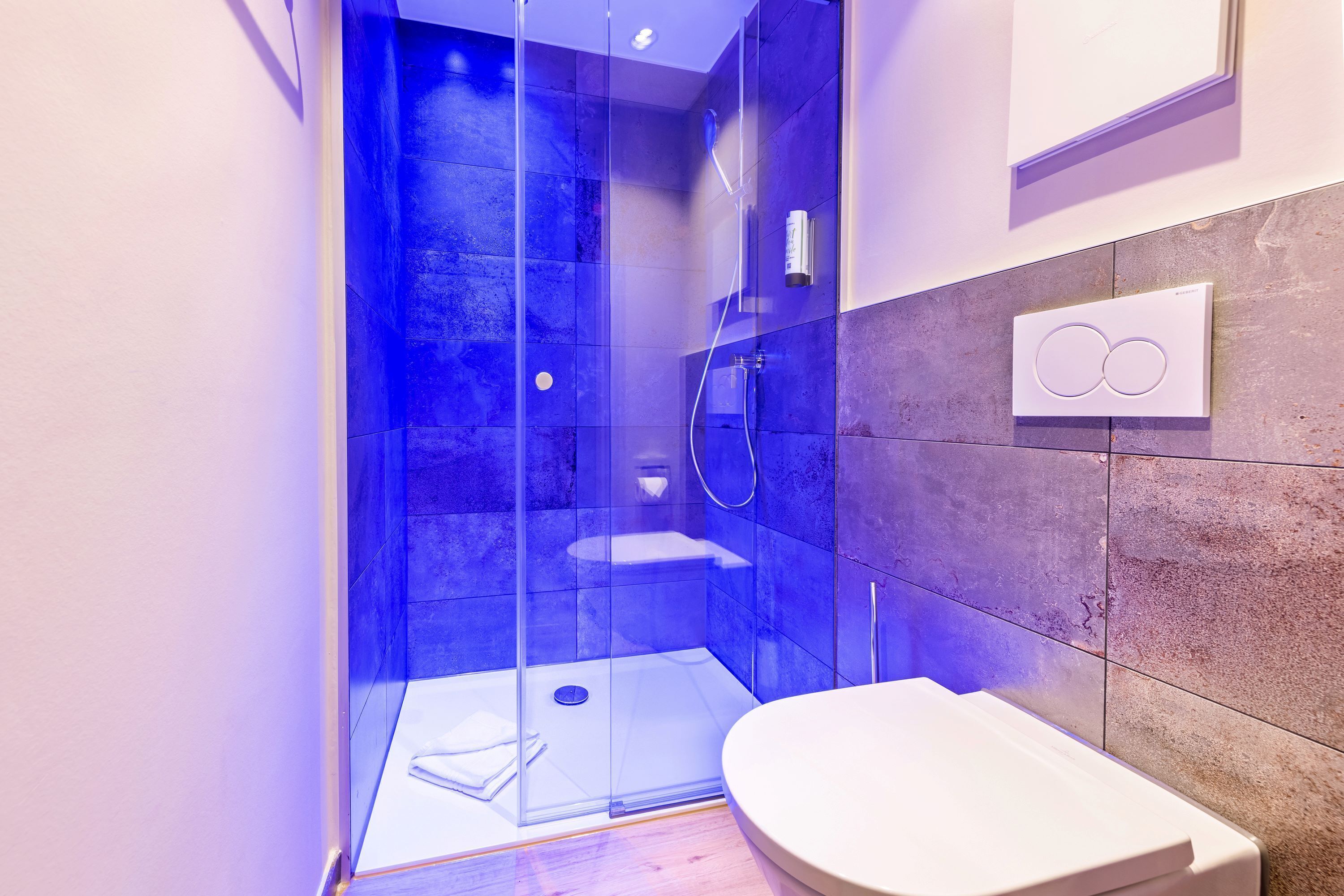 A modern bathroom with a glass-enclosed shower, a white toilet, and a wall-mounted towel dispenser.