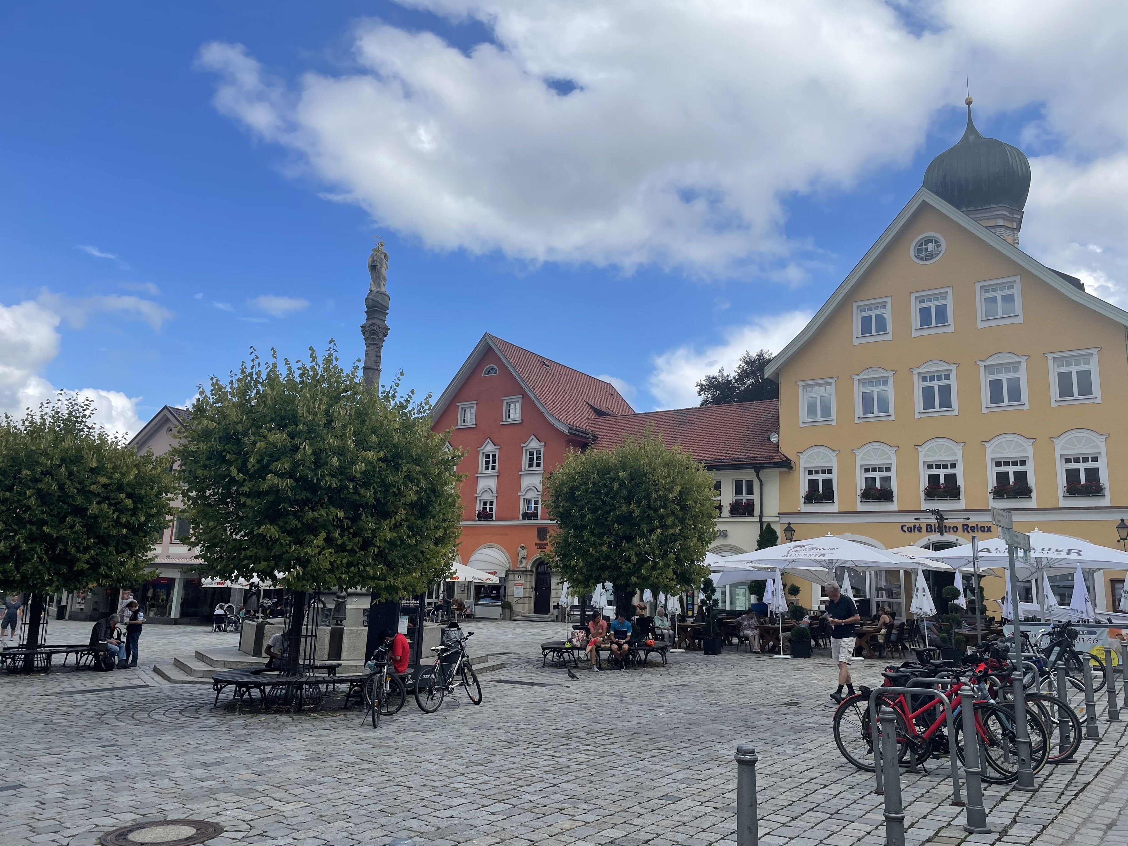Uma praça de pedra com mesas ao ar livre, bicicletas e um edifício histórico com uma torre do relógio.
