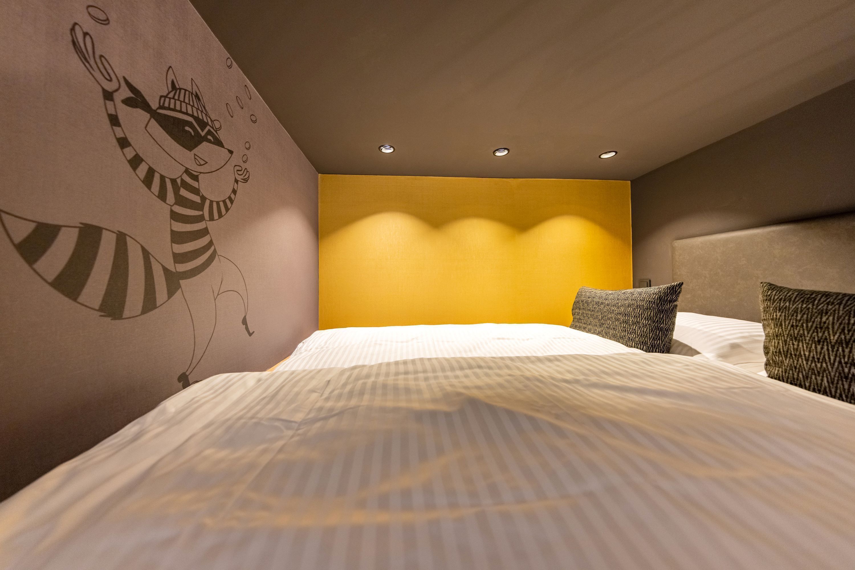 A hotel room with a large bed, a headboard with built-in lighting, and a wall mural of a raccoon.