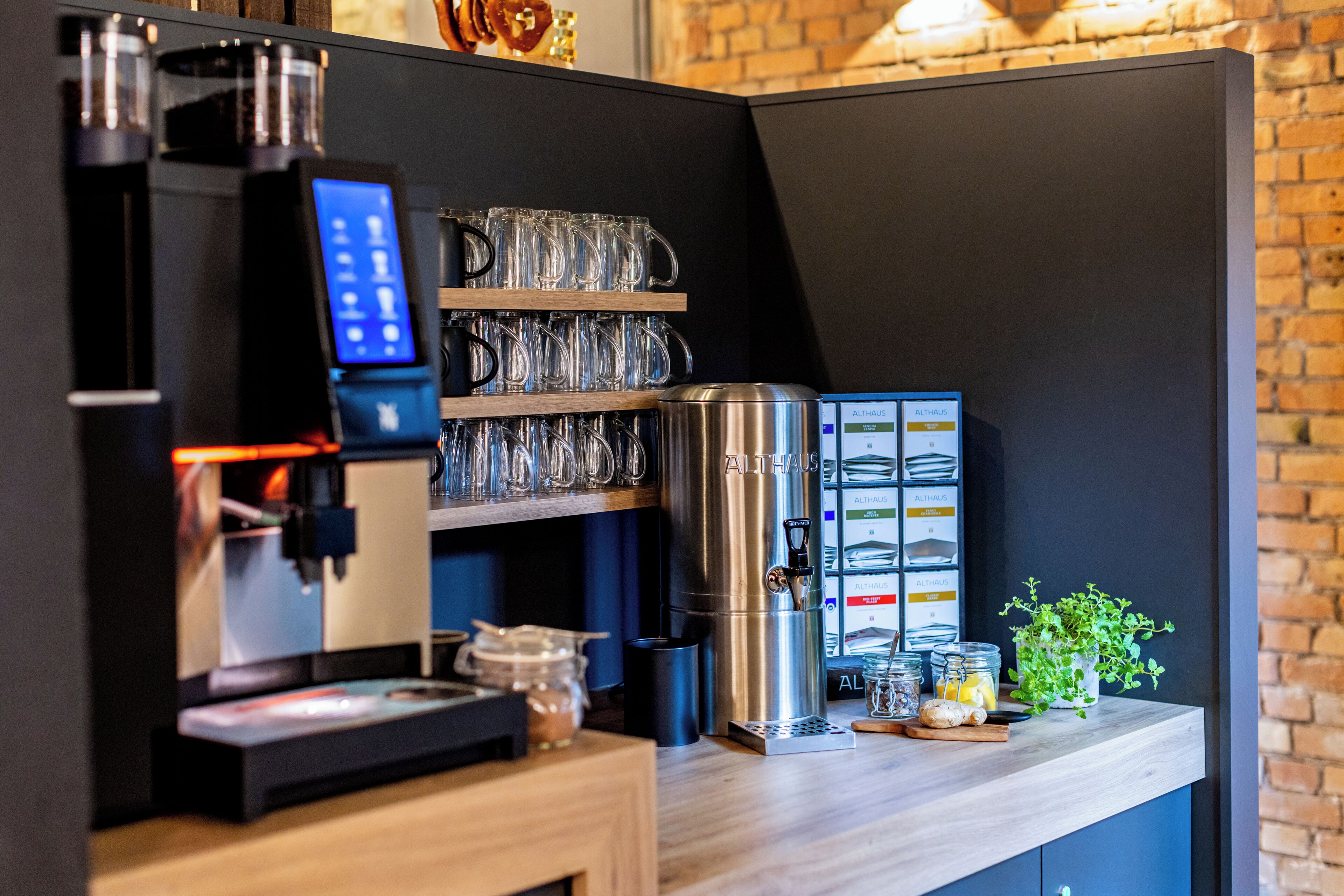 A coffee machine, glass mugs, a stainless steel container, and a potted plant on a wooden counter.