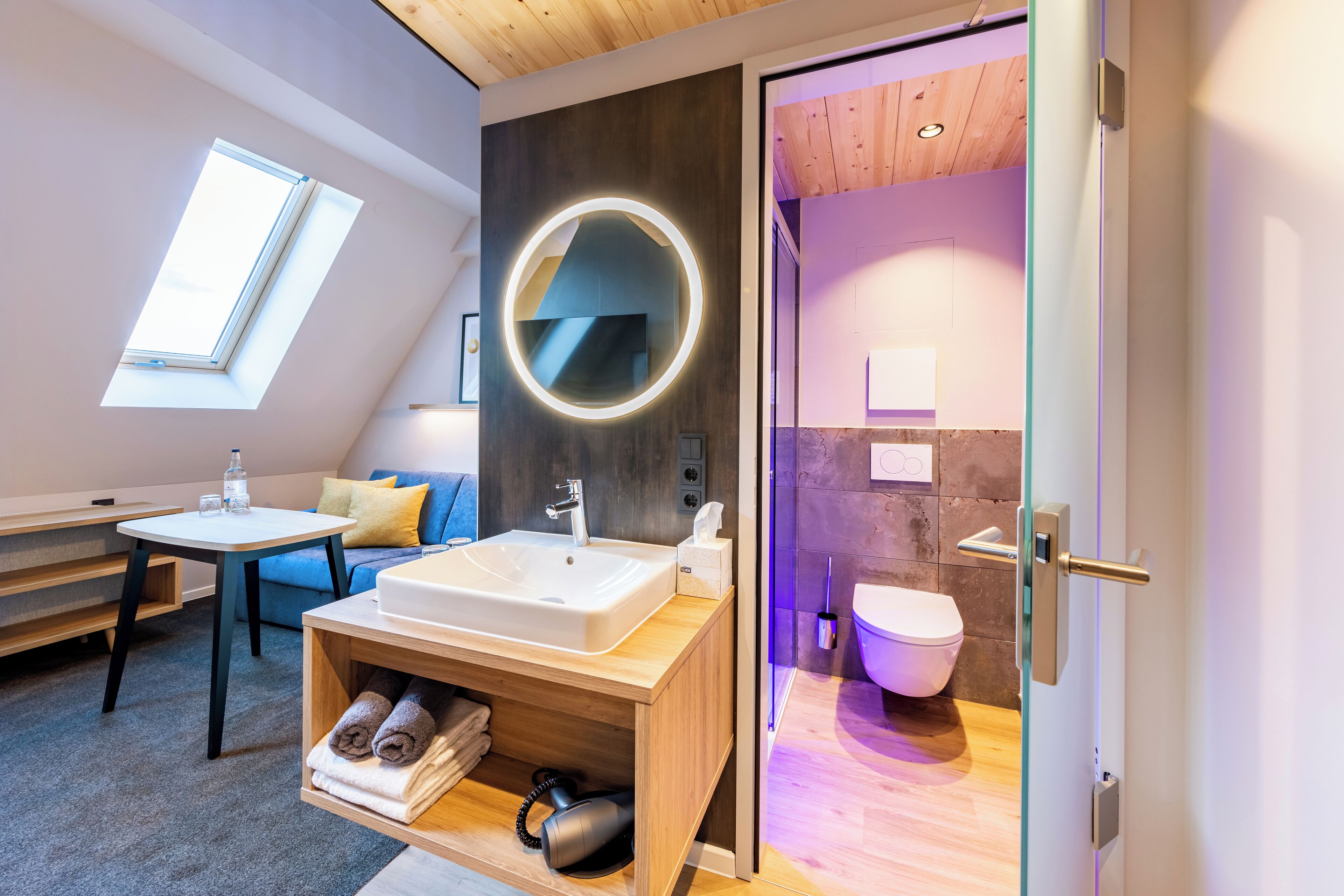Un baño moderno con tragaluz, un espejo redondo, un lavabo y un inodoro.