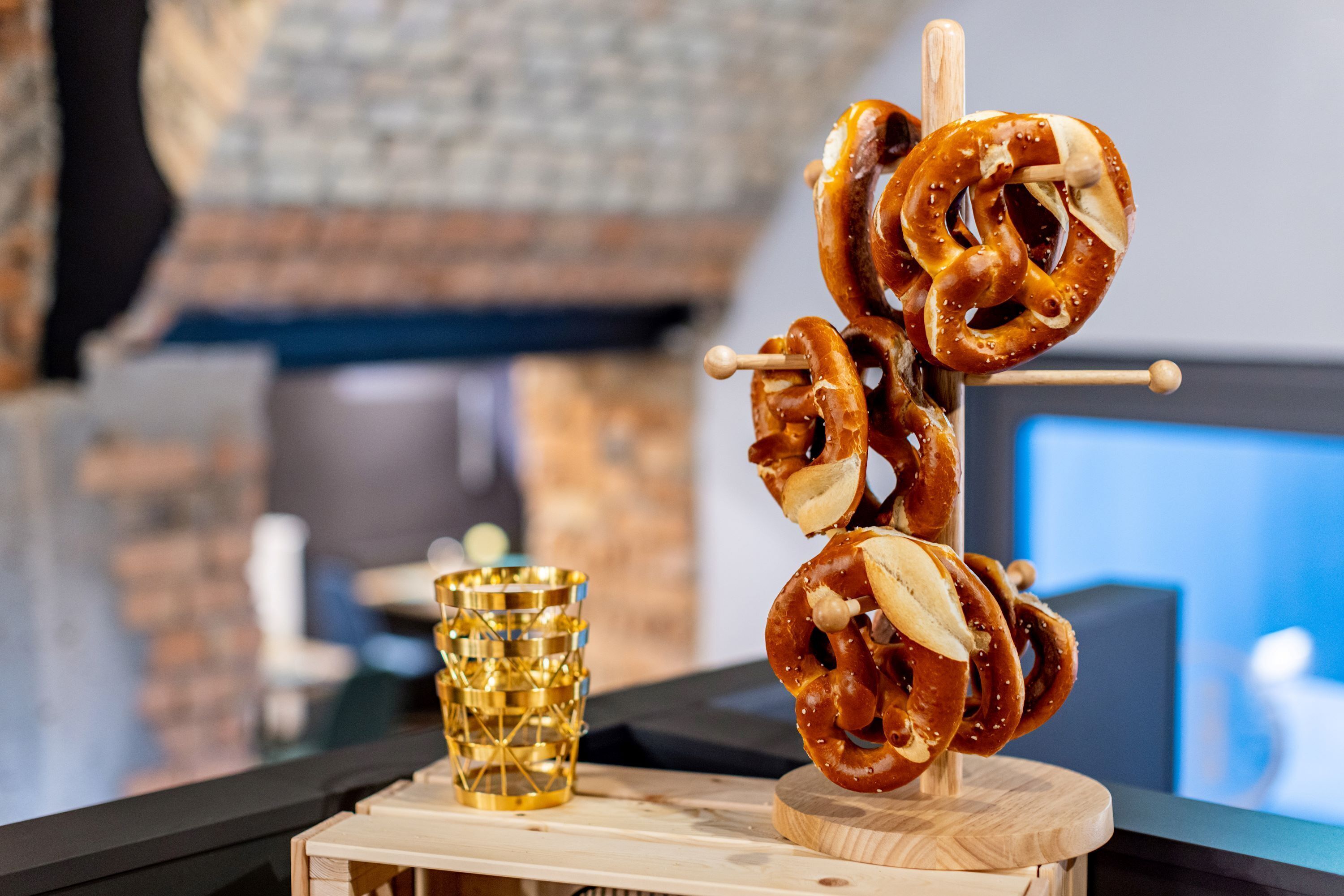 Um suporte de madeira com pretzels e um copo dourado ao lado.