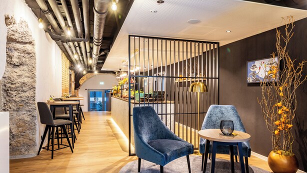 A modern interior with a wooden floor, a blue velvet chair, a small round table, and a decorative plant. - BOLLWERK Lifestyle Hotel - automatisiertes Hotel mit Self Check In (Immenstadt im Allgaeu)