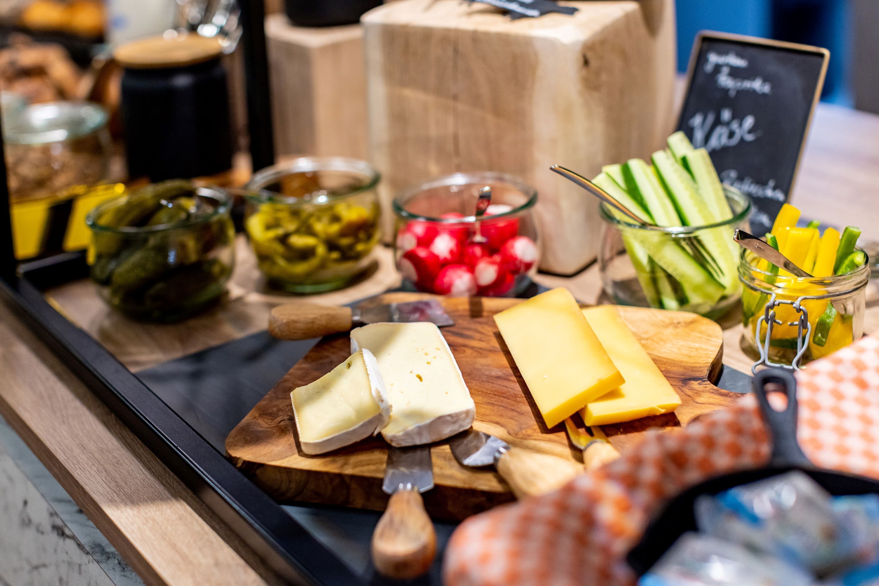 A cheese and charcuterie board with various cheeses, pickles, and vegetables.
