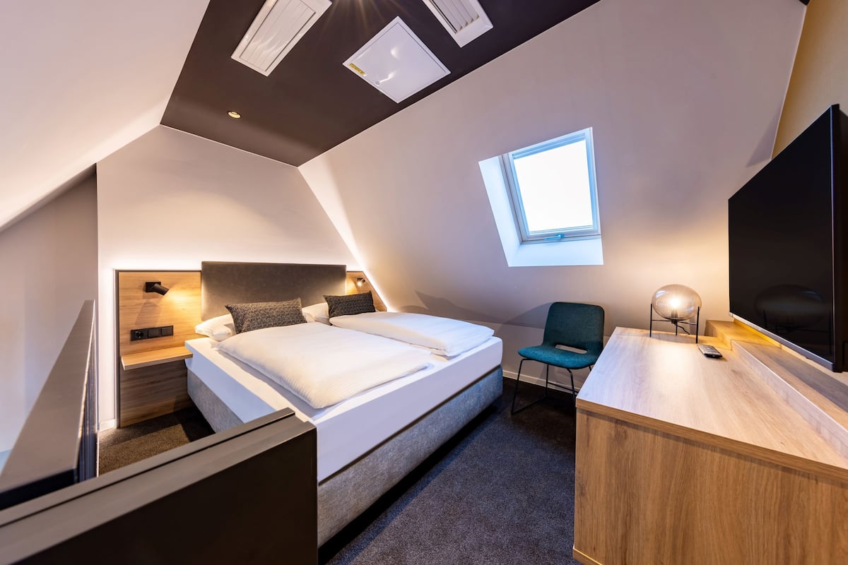 A modern hotel room with a large bed, a desk, a chair, and a TV.
