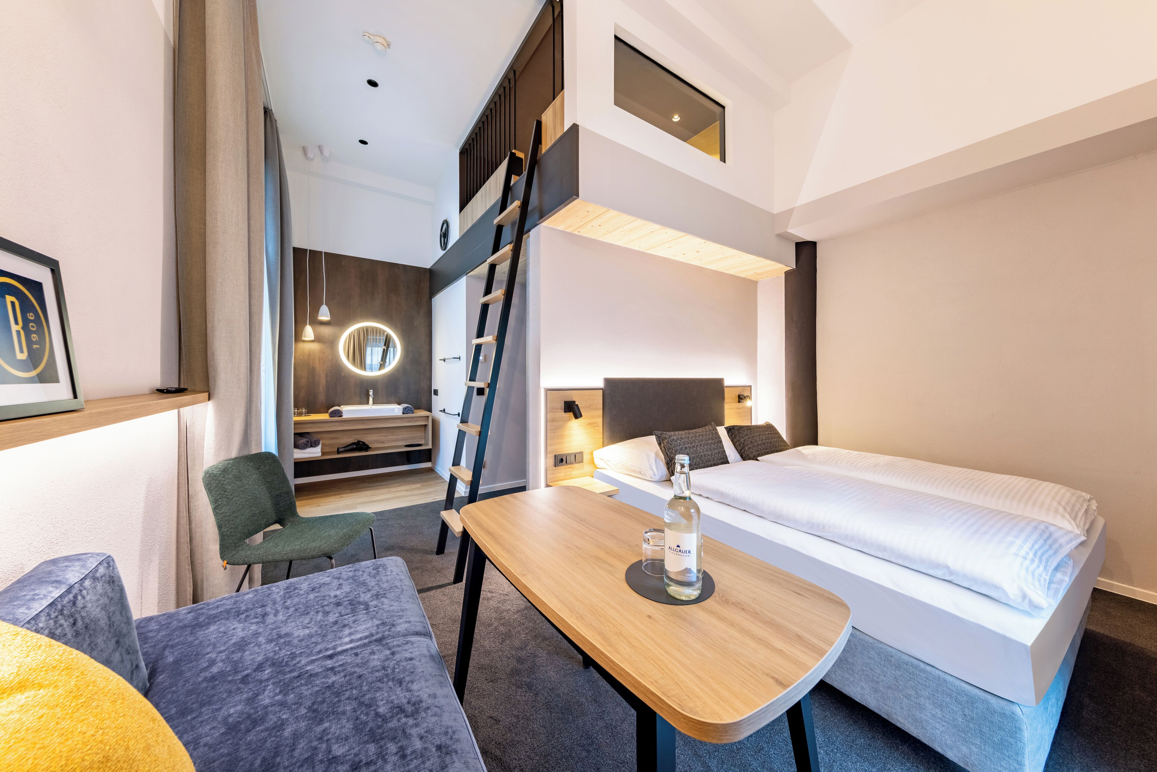Ein modernes Hotelzimmer mit Bett, Schreibtisch, Stuhl und einer kleinen Küchenzeile.