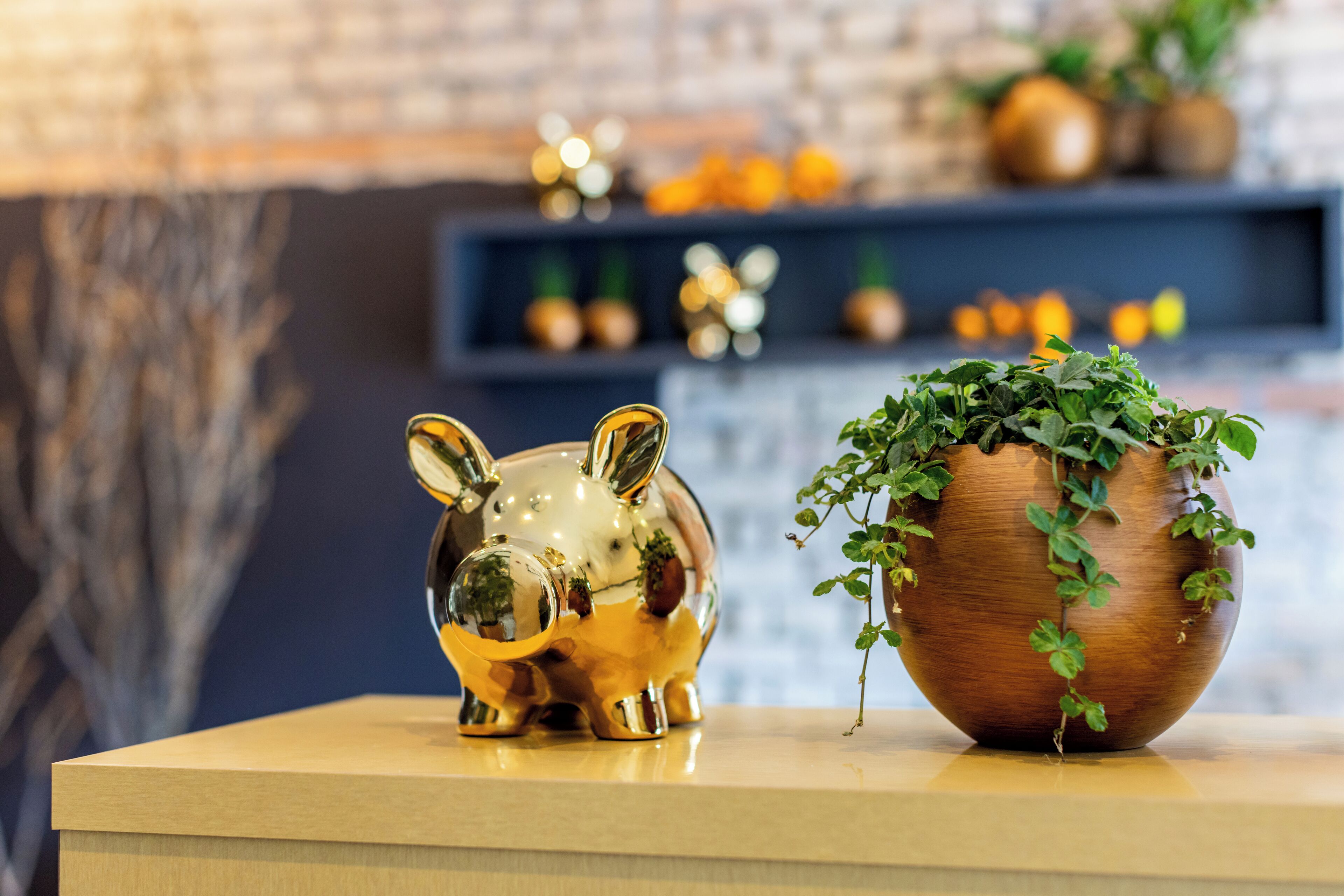 A gold piggy bank and a wooden planter with green plants on a wooden surface.