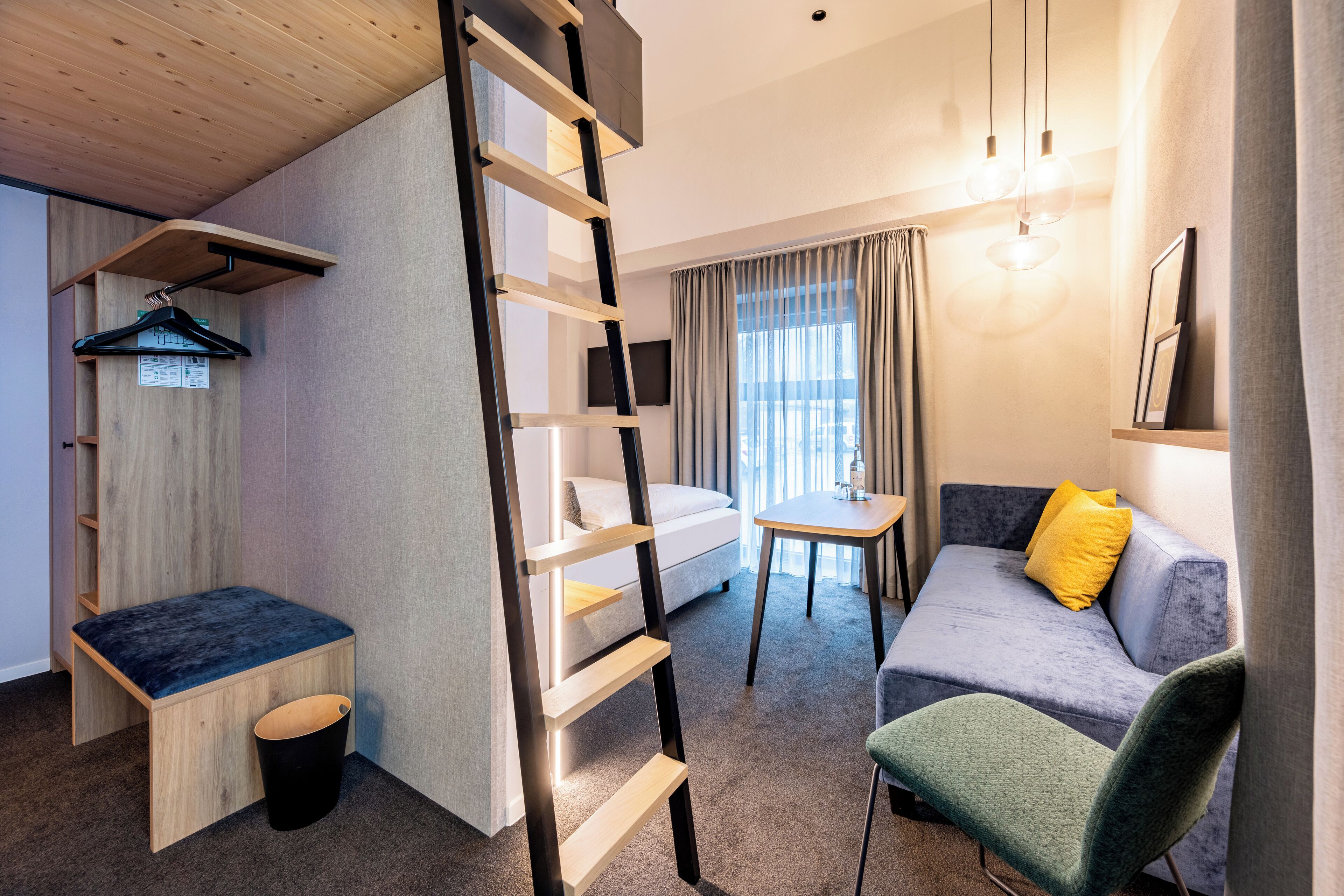 Ein modernes Hotelzimmer mit Schlafgalerie, Schreibtisch, einer Couch und einem Sessel.