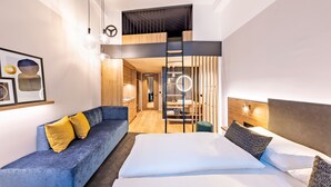A modern hotel room with a bed, a sofa, a mirror, and a bathroom visible through a partition. - BOLLWERK Lifestyle Hotel - automatisiertes Hotel mit Self Check In (Immenstadt im Allgaeu)