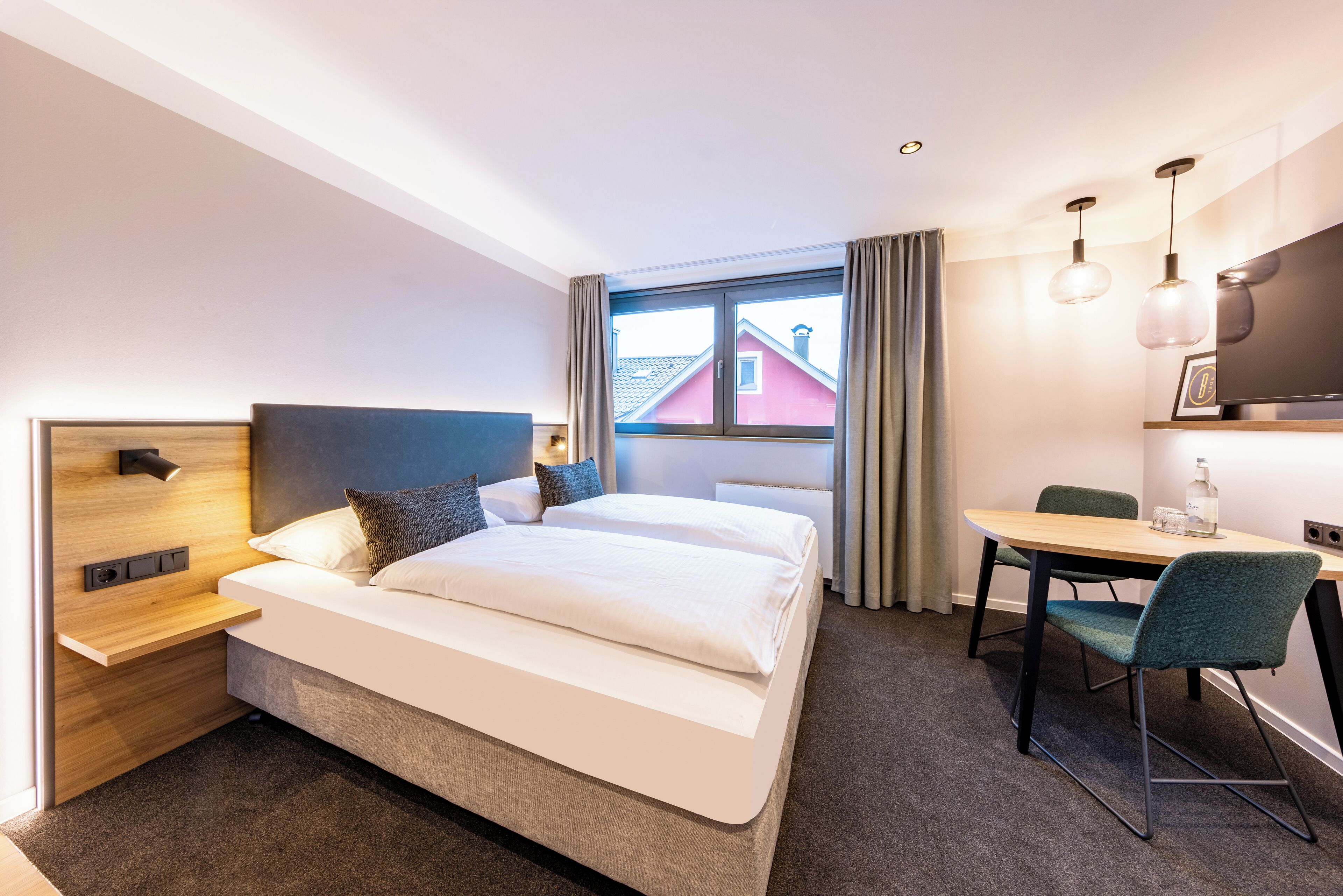 Een hotelkamer met een bed, nachtkastje, lamp, bureau, stoel en een televisie.