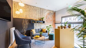 A modern lounge area with a brick wall, a sofa, a round coffee table, and a TV mounted on the wall. - BOLLWERK Lifestyle Hotel - automatisiertes Hotel mit Self Check In (Immenstadt im Allgaeu)