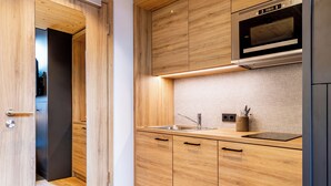 A modern kitchen with wooden cabinetry, a stainless steel sink, and a microwave above the countertop. - BOLLWERK Lifestyle Hotel - automatisiertes Hotel mit Self Check In (Immenstadt im Allgaeu)