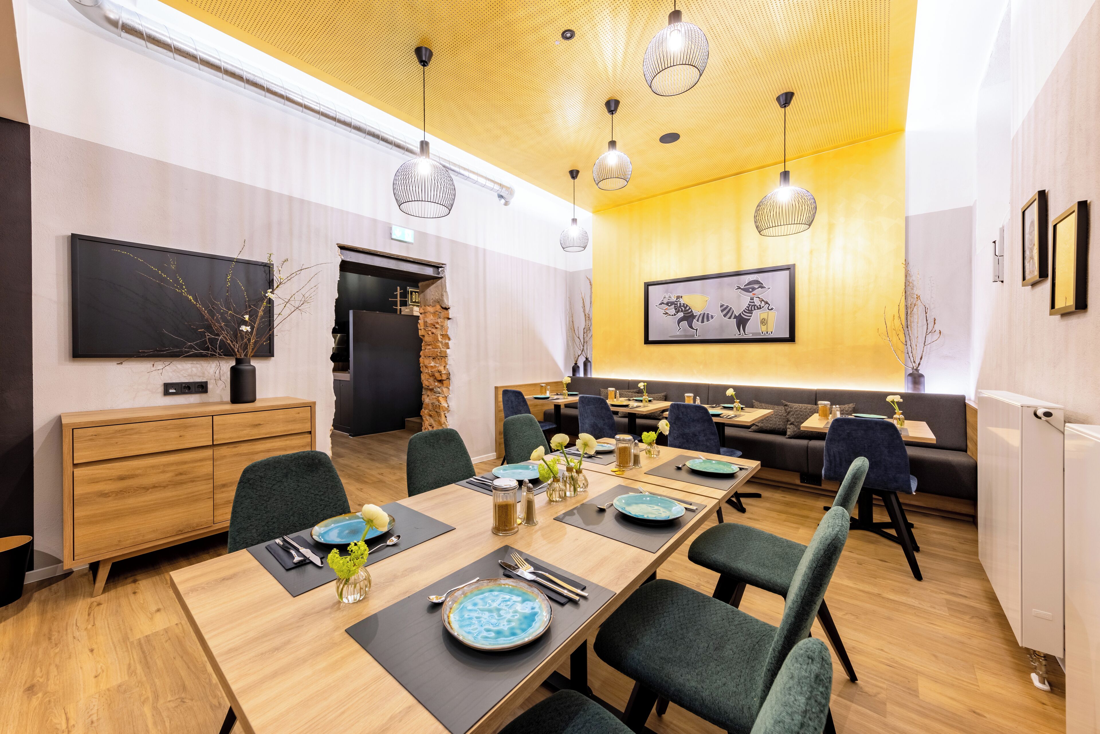 A modern dining area with wooden tables, green upholstered chairs, and pendant lighting.