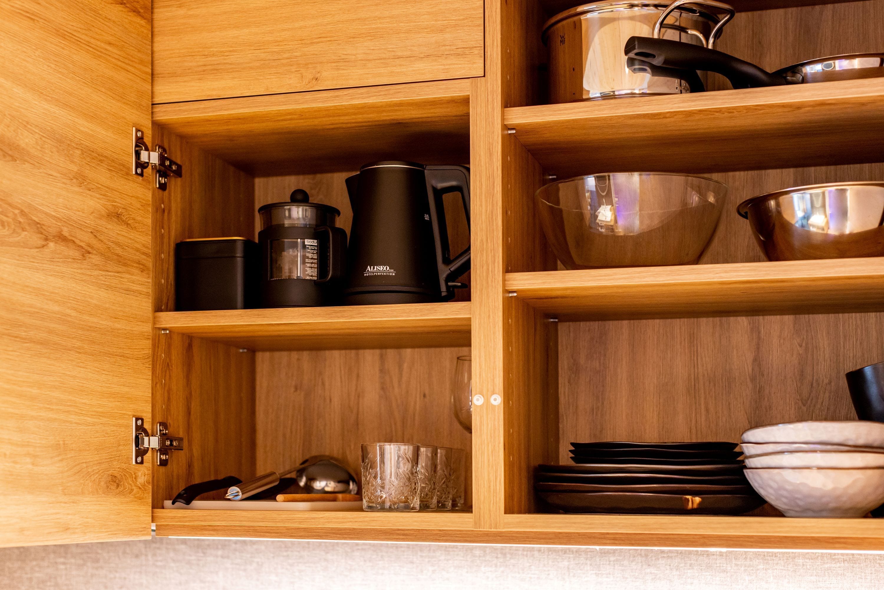 Un pensile in legno con ripiani contenenti utensili da cucina, tra cui pentole, una macchina per il caffè e bicchieri.