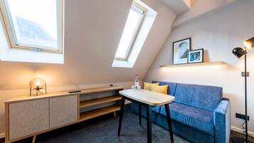 A modern loft bedroom with skylights, a blue sofa, a small table, and a desk with a lamp.