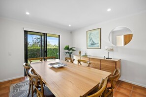 A dining area with a wooden table and chairs, a sideboard, and a large window with a view of greenery.