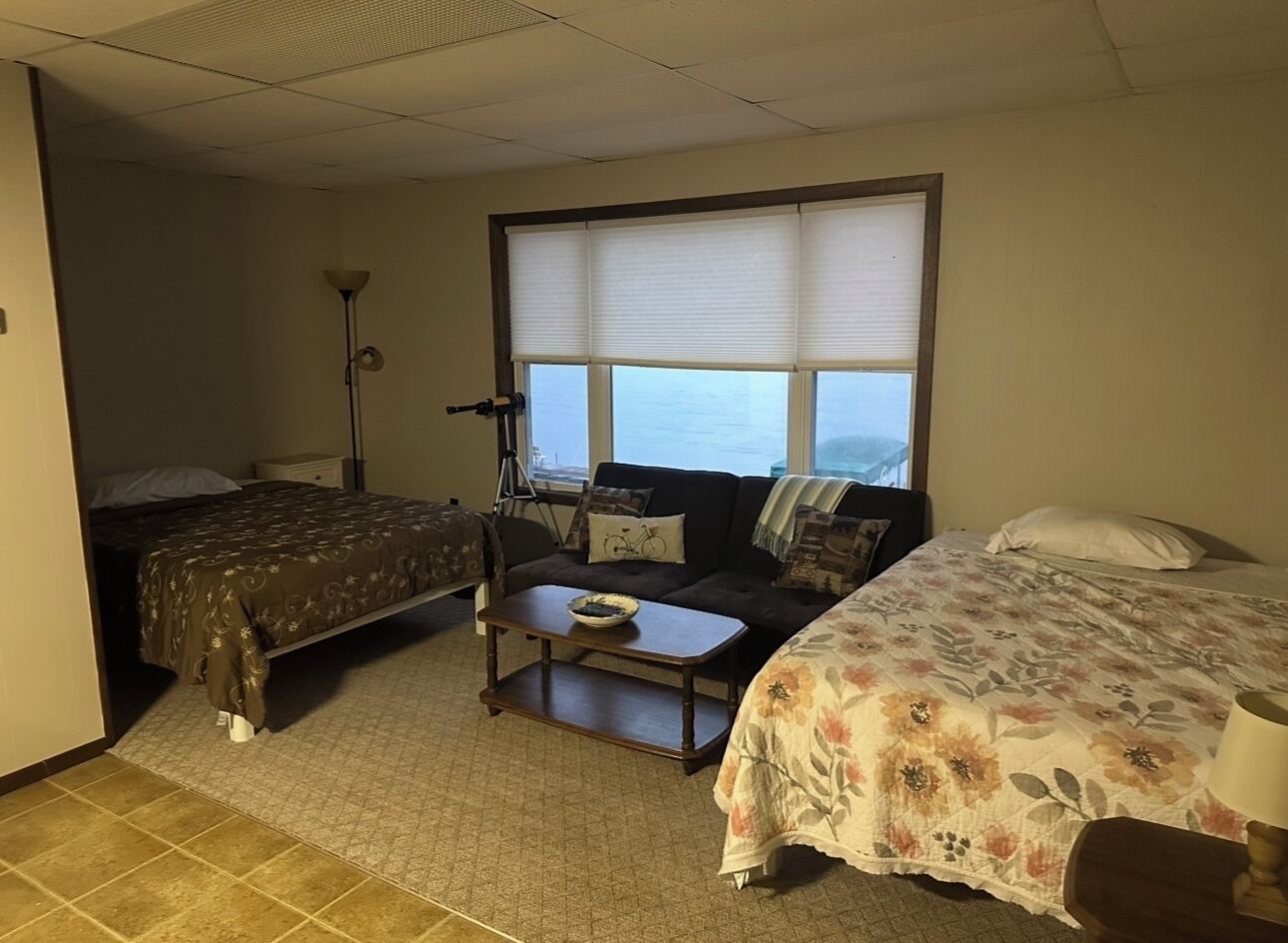 A hotel room with two beds, a sofa, a small table, and a window with blinds.
